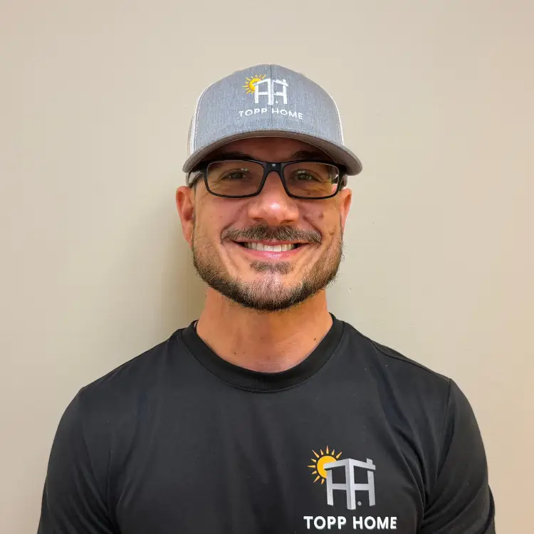 Smiling man wearing a gray cap and black T-shirt with the TOPP HOME logo against a neutral wall. - My Topp Home
