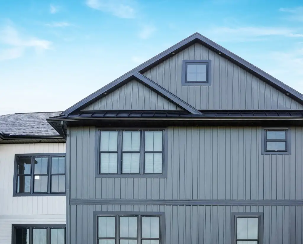 Front view of a gray-blue house with a steep peaked roof, vertical siding, and multiple rectangular windows - My Topp Home